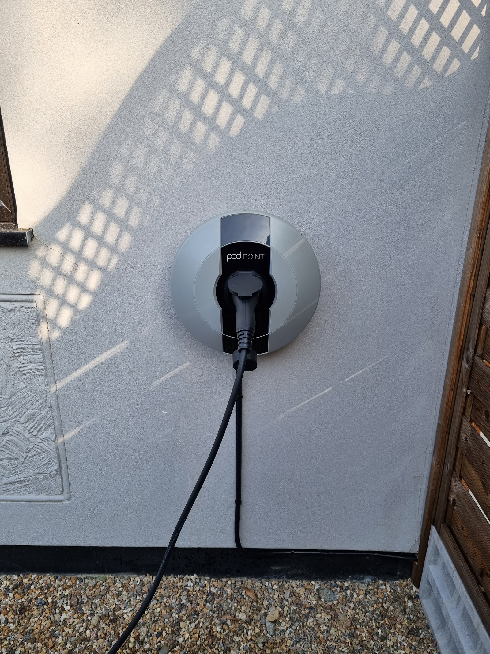 Pod Point home charger mounted to a rendered wall, supply run down neatly to the isolator and connector holstered.